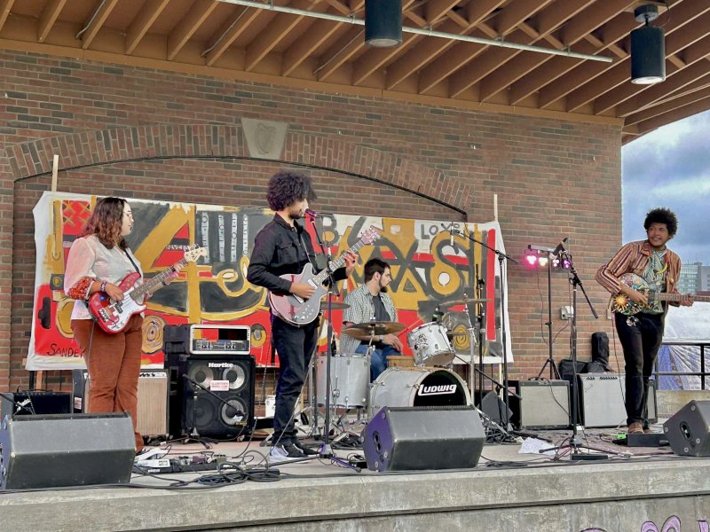 A band performing on an outdoor stage with a brick wall behind them