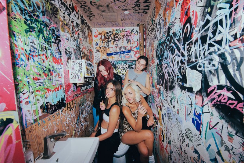 Four people sitting together in a small bathroom with graffiti covering the walls