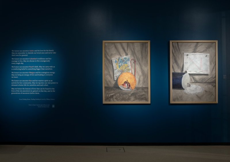 Installation view of a vinyl wall text treatment and two oil painting still lifes to the right of it