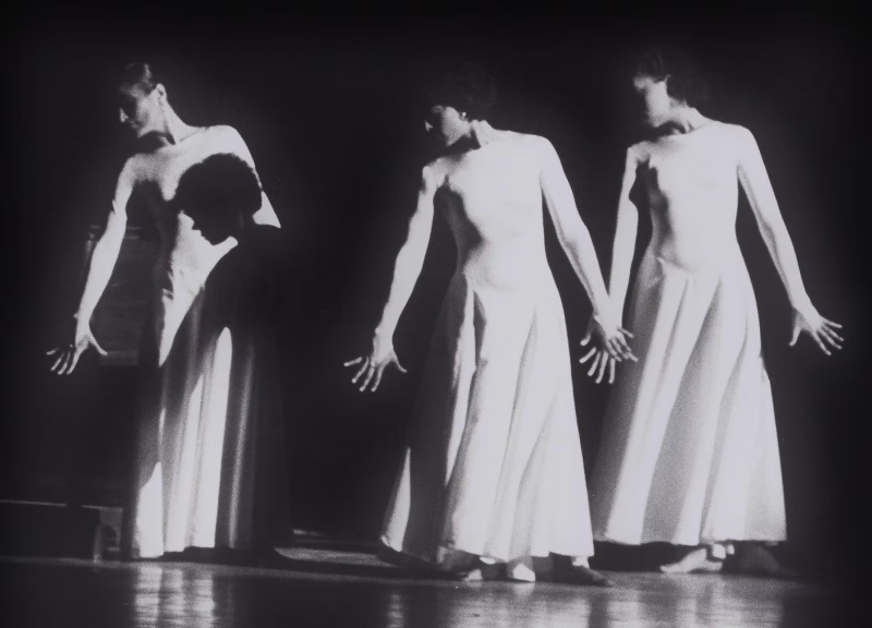 Three women in white dresses dancing with their arms at their sides