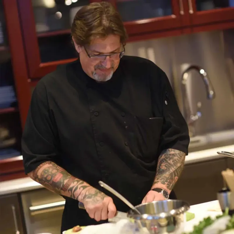 A man with tattoos cutting vegetables at a kitchen counter