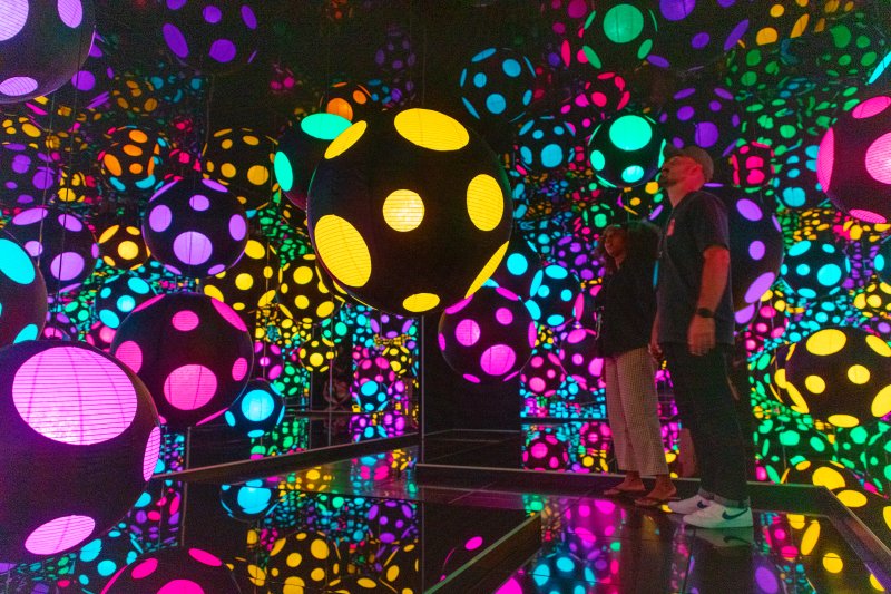 Two individuals in a room of mirrors and vibrantly-lit circles