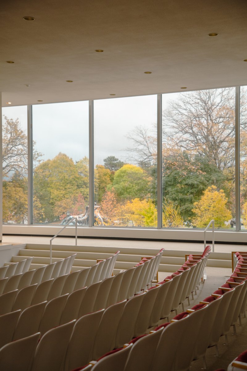 Rows of auditorium chairs and a view out of a glass wall onto colorful trees