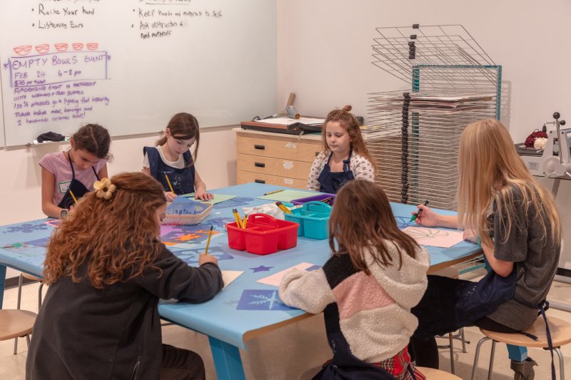 A group of children working on art projects around a blue square table in a studio