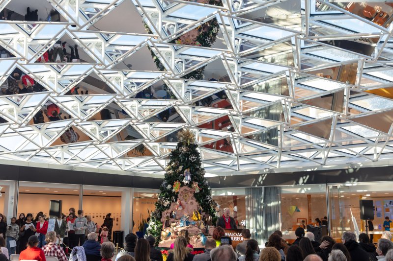 A crowd gathered around a large Christmas tree under a glass mosaic ceiling