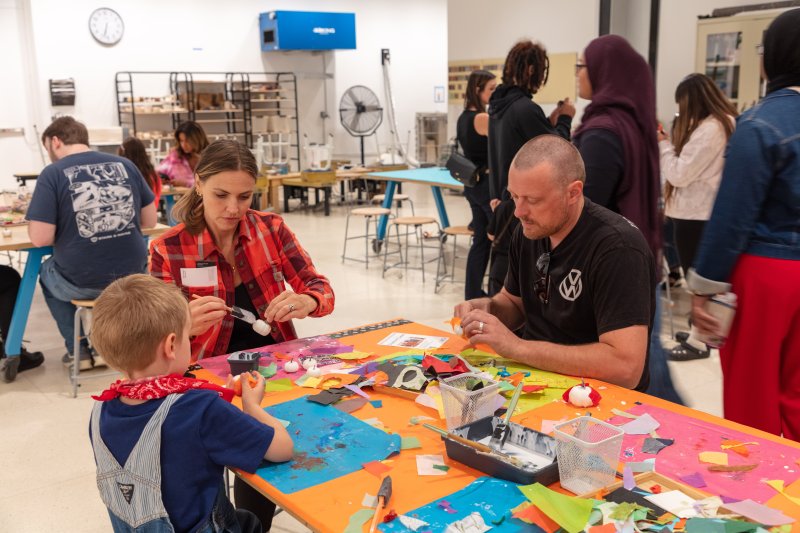 A man, a woman, and a child working on an artmaking activity with brightly colored materials