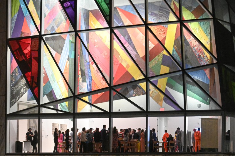 A crowd inside a glass building with a multi-patterned swath of fabric draped on the ceiling
