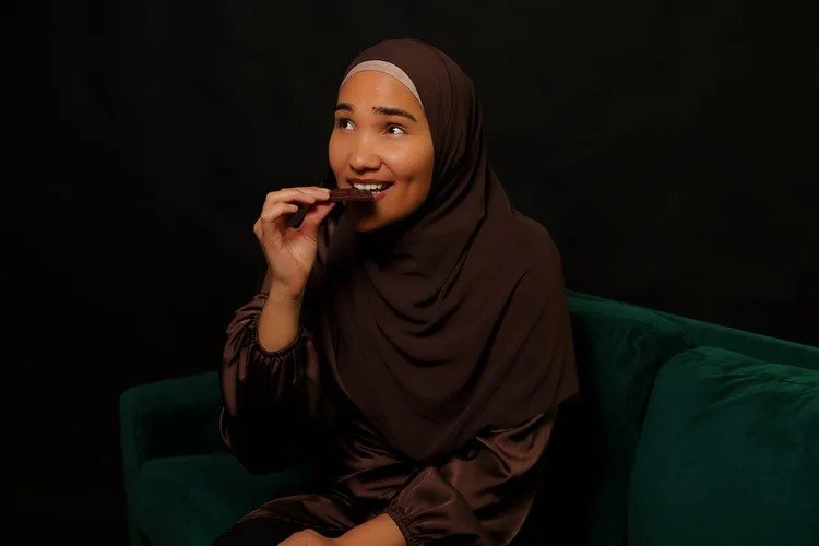 An image of a woman with a headcovering enjoying a small piece of chocolate