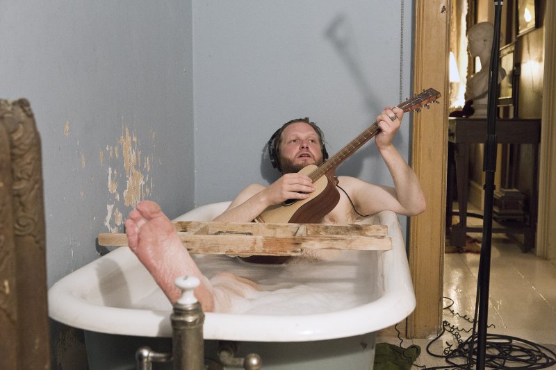 A person playing a guitar in a clawfoot bathtub 
