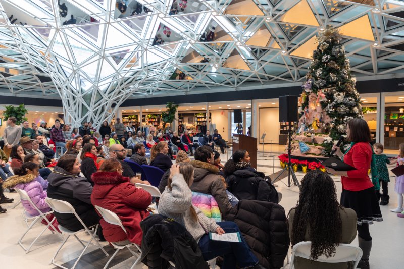 People gathered around a large Christmas tree under a glass mosaic ceiling
