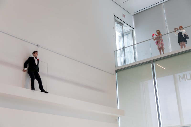 A man in a tuxedo standing on a ledge against a white wall