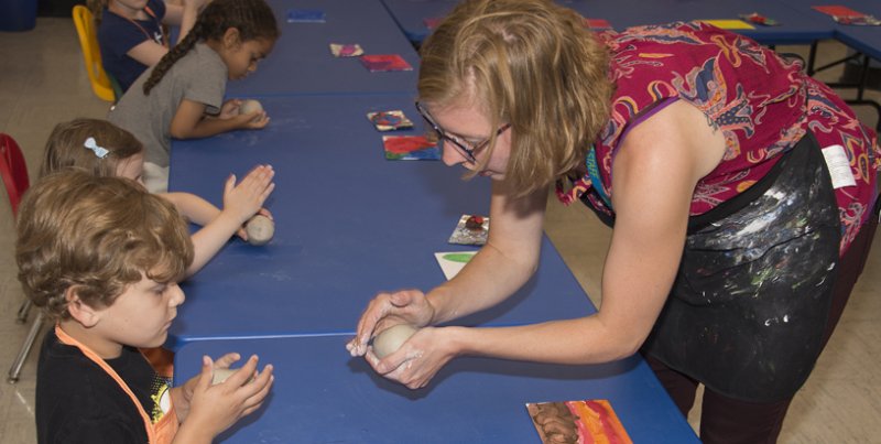 An instructor assist a young child with a ceramics project