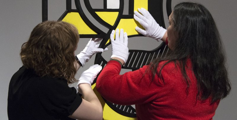 A tour guide and visitor touching a sculpture with white gloves on.
