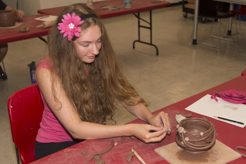 A young woman decorates an unfired clay pot