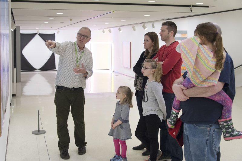 Visitors of all ages listen to a docent talk about an artwork in the 1962 Building