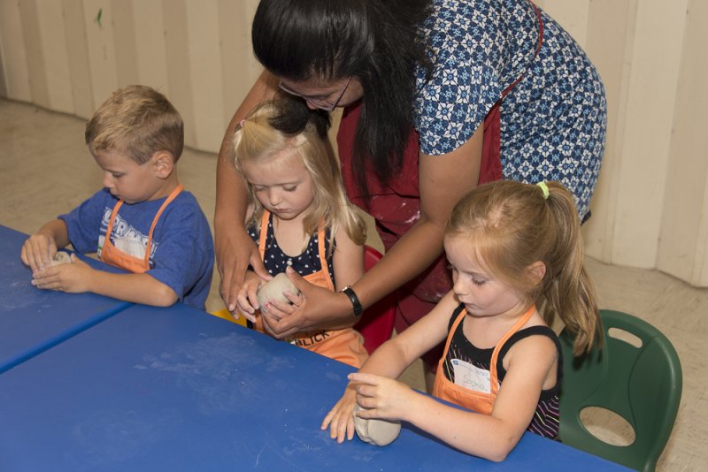 A teacher helping young kids sculpt with clay