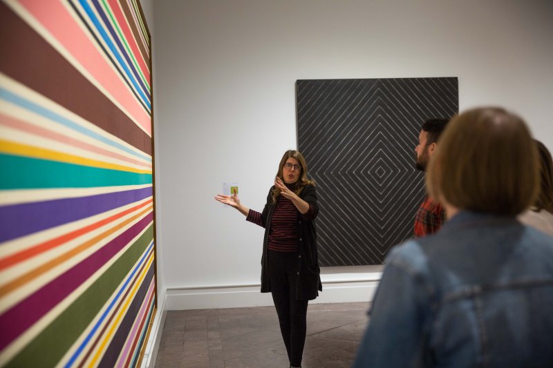 An adult woman giving a tour in front of Ken Noland's painting Wild Indigo