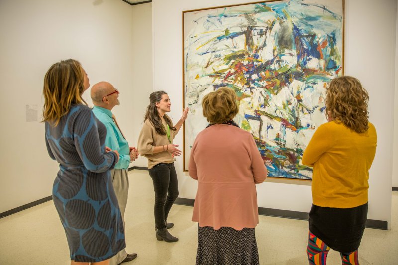 Adults on a tour in front of an abstract painting by Joan Mitchell with blue and green strokes on a white background