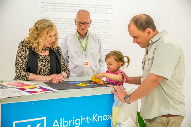 A young girl, a man, and a volunteer docent play with materials on the ArtCart