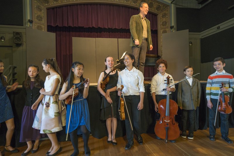 Students holding their instruments standing in front of a stage