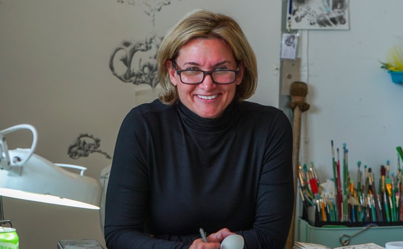 A woman with chin-length blonde hair and glasses wearing a black turtleneck