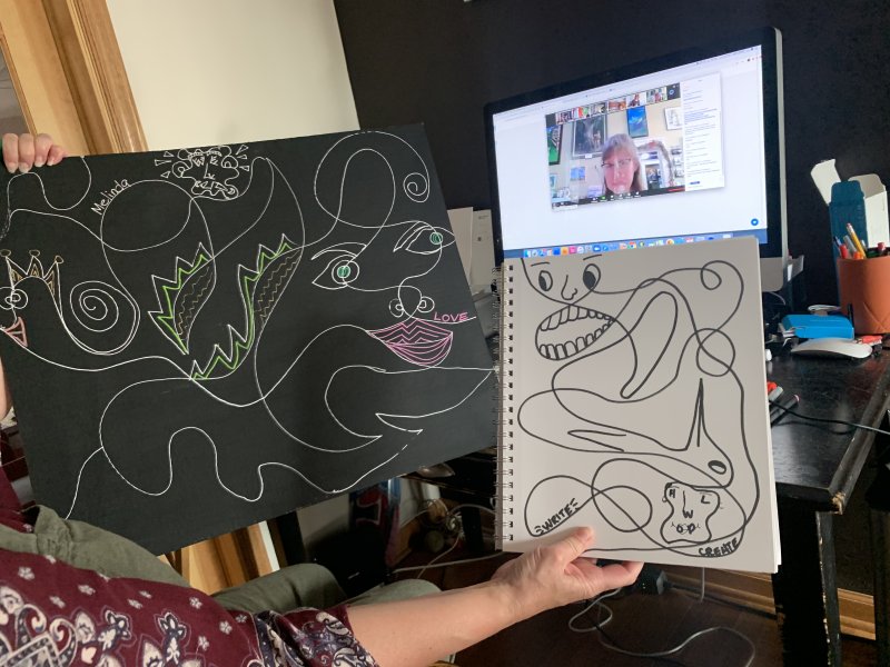 A person holding up drawings in front of a computer screen