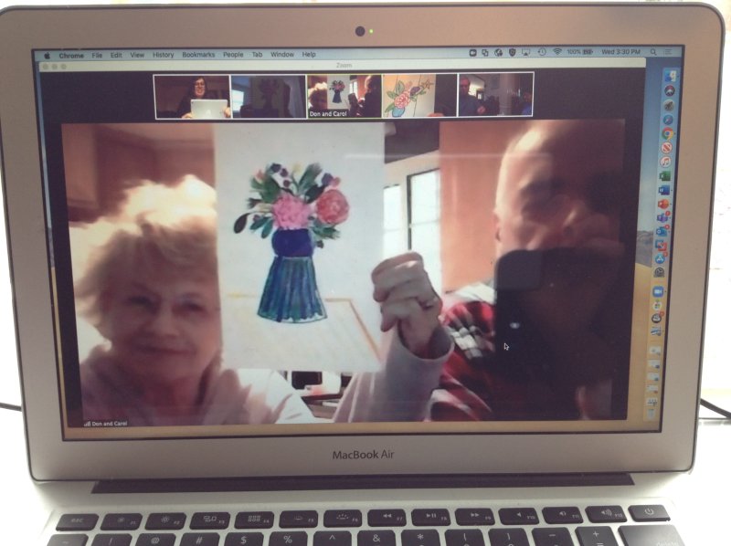 A woman and man holding up a print of flowers in a vase on a computer screen
