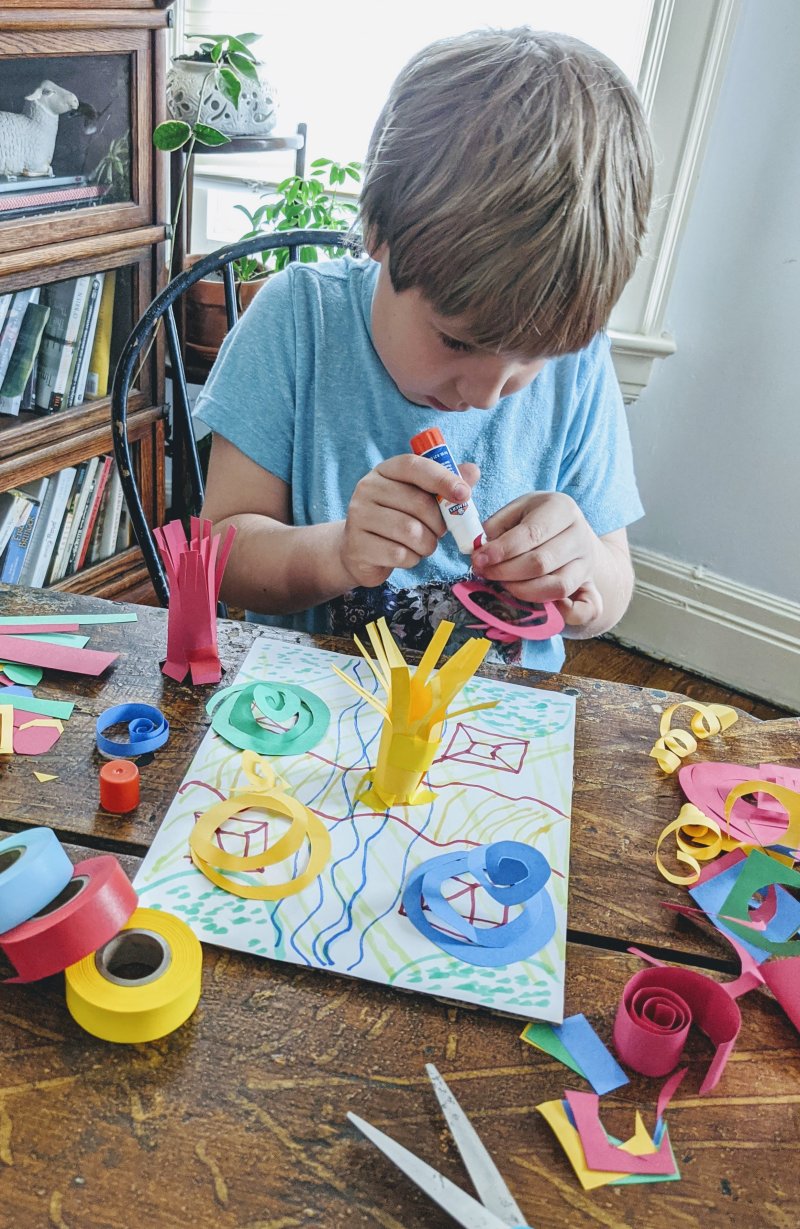 A boy gluing paper shapes to a piece of cardstock