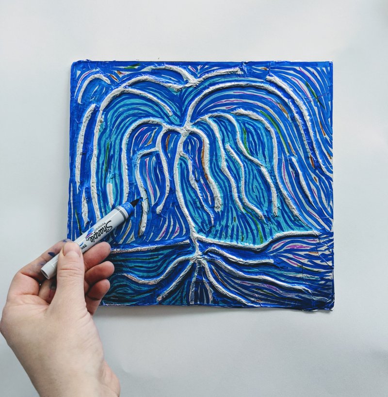 A person coloring a blue background around a shiny silver foil tree
