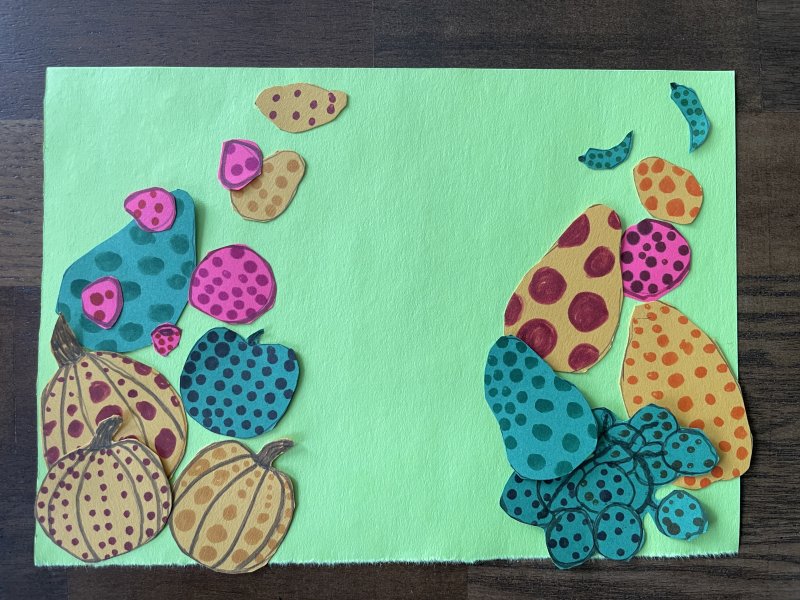 Pumpkins and other fruit decorated with dots and arranged on a green piece of construction paper