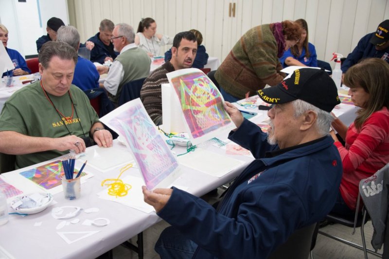 Adult men and women sitting around tables in a classroom working on an art project