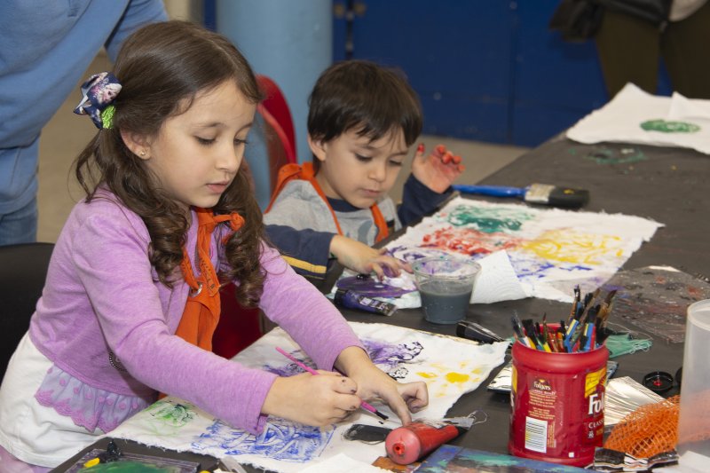 A young girl and boy applying colored paint to white fabric