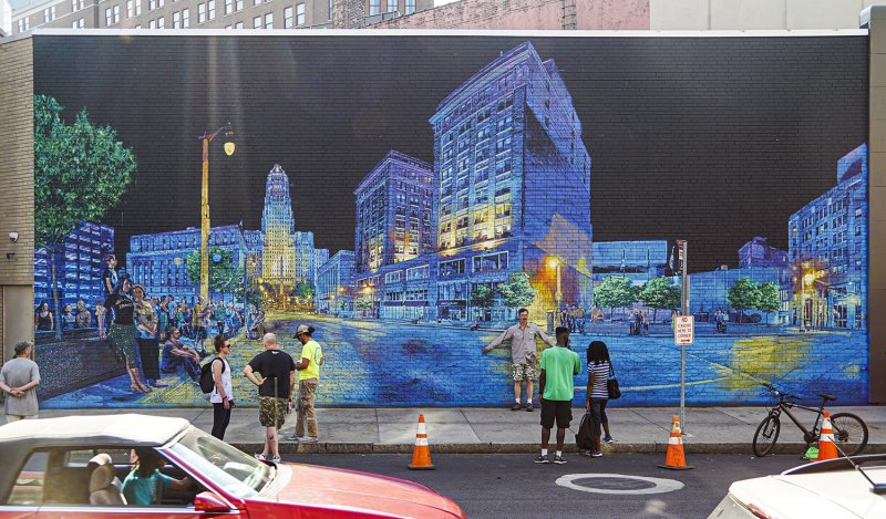 People standing in front of a mural of buildings painted in blues, greens, and yellows on a black background