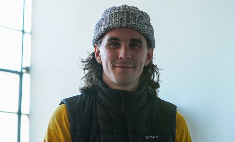 A headshot of a man with long hair and a hat