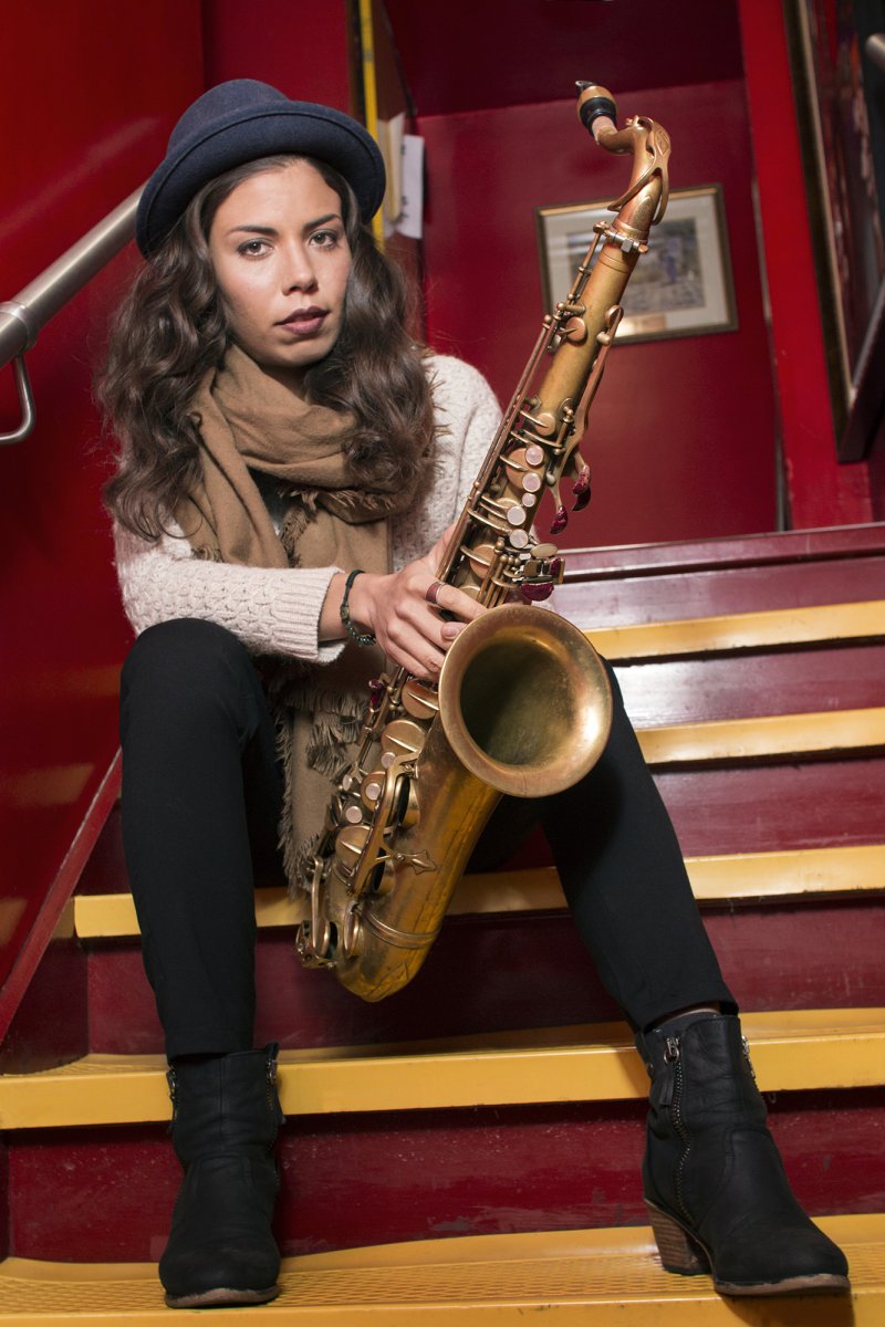 Melissa Aldana sitting on steps holding her saxophone