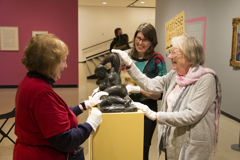 A tour guide and visitors touching a sculpture with white gloves on