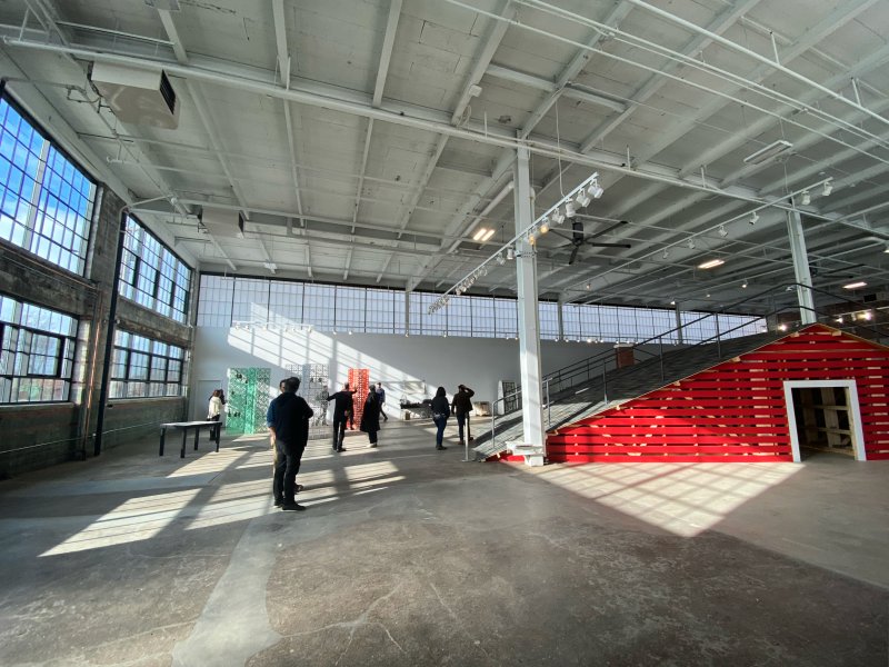 A large industrial building with a rooftop inside of it and colorful wooden screens holding clear and green glass bottles
