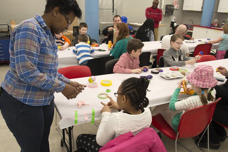 A woman bends over a table to help a child with an art project