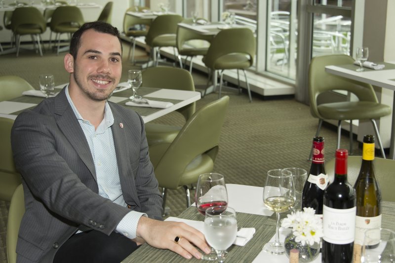 A man sits at a table in AK Cafe with a glass of water and several bottles of wine