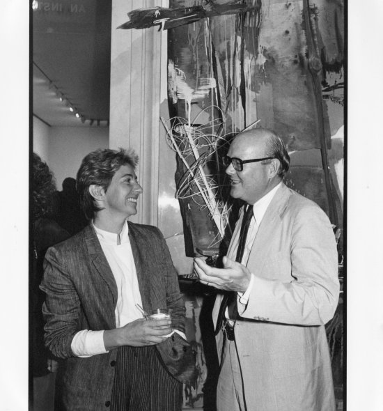 Black and white image of two people talking in front of an art installation