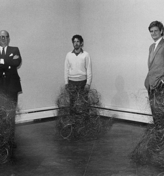 Black and white image of three men standing in front of knee-length sculptural objects