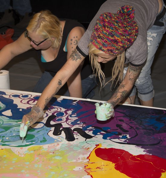 Two women applying paint to a large canvas on the floor