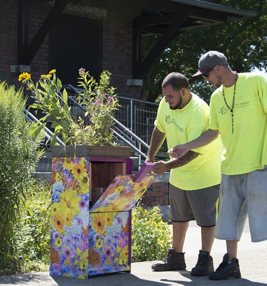 Two men in yellow shirts open an honor box covered in a floral design