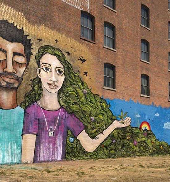 Mural on a red brick building of a man with dark skin and a woman with light skin and long green hair