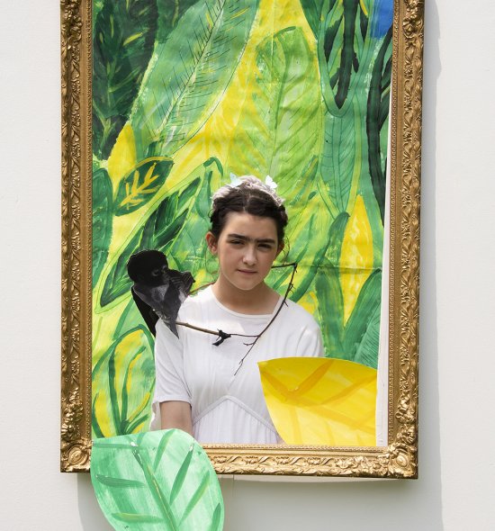 A girl with a stuffed monkey on her shoulder standing in front of a green painted backdrop