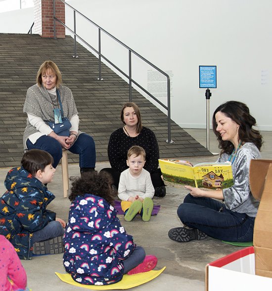A woman reads a book to a group of children sitting on the floor