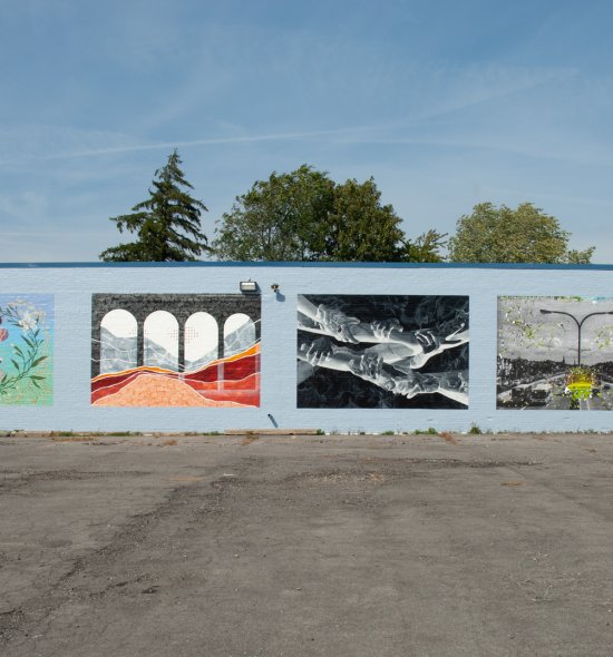 Six colorful murals on a long gray exterior wall