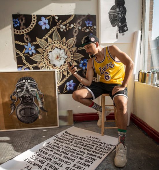 Man of medium-light skin tone in yellow basketball jersey sits on stool studio a long scroll at his feet, digital photographs in the background