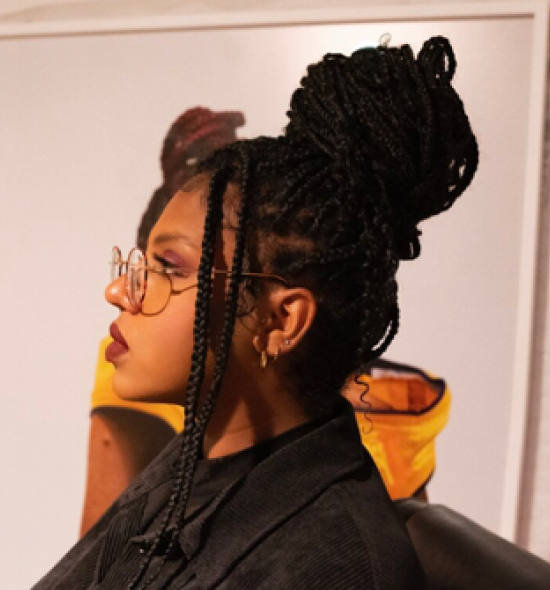 Woman of medium-dark skin tone with braids in black shirt in profile looks left