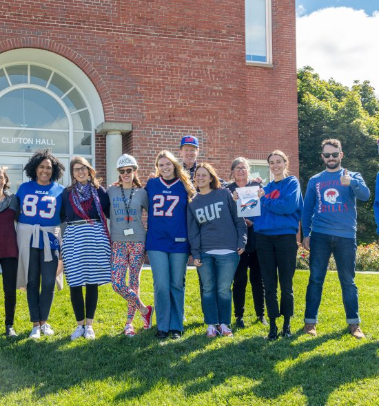 Group of Buffalo AKG staff members posing outside of Clifton Hall with their Buffalo Bills gear 
